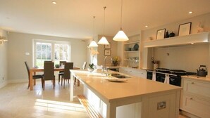A modern kitchen with a central island, pendant lighting, and a dining area with a view of the outdoors. - Hillside Cottage (Burford)