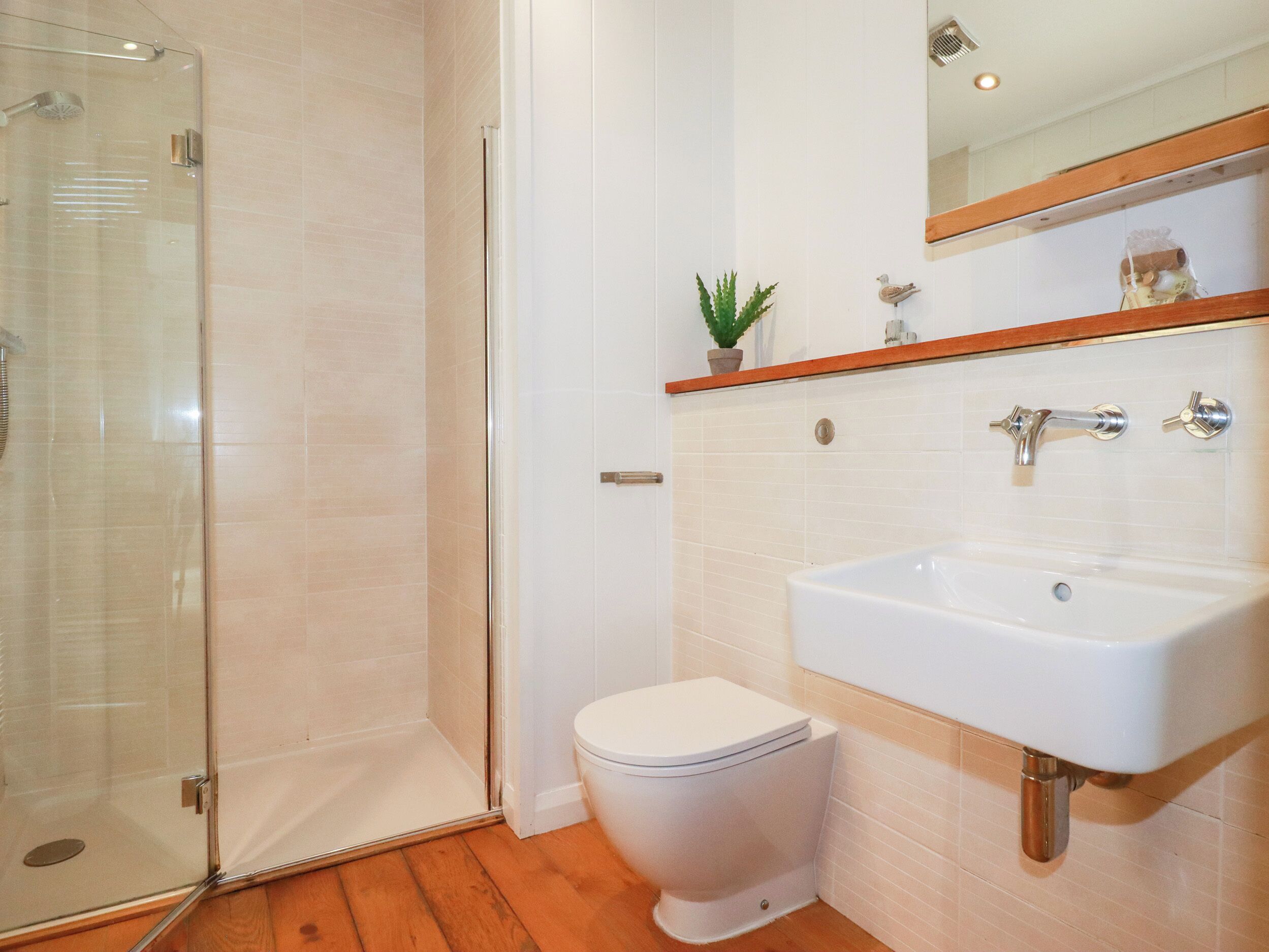Ein Badezimmer mit Duschkabine aus Glas, einer weißen Toilette und einem Waschbecken mit Spiegel darüber.