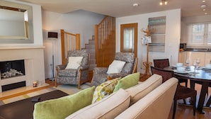 A living room with a fireplace, a sofa, a chair, a dining table set for four, and a staircase leading to another level. - 4 Dart Marina (Dartmouth)