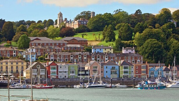 A coastal town with colorful houses, a marina with boats, and a prominent building on a hill. - 4 Dart Marina (Dartmouth)