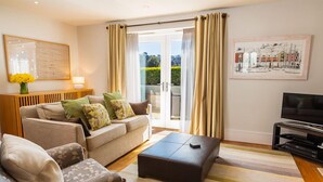 A living room with a sofa, ottoman, and armchairs, a flat-screen TV, and a painting on the wall. - 4 Dart Marina (Dartmouth)