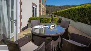 A round glass table with wicker chairs, a glass door, and a view of a hillside. - 4 Dart Marina (Dartmouth)