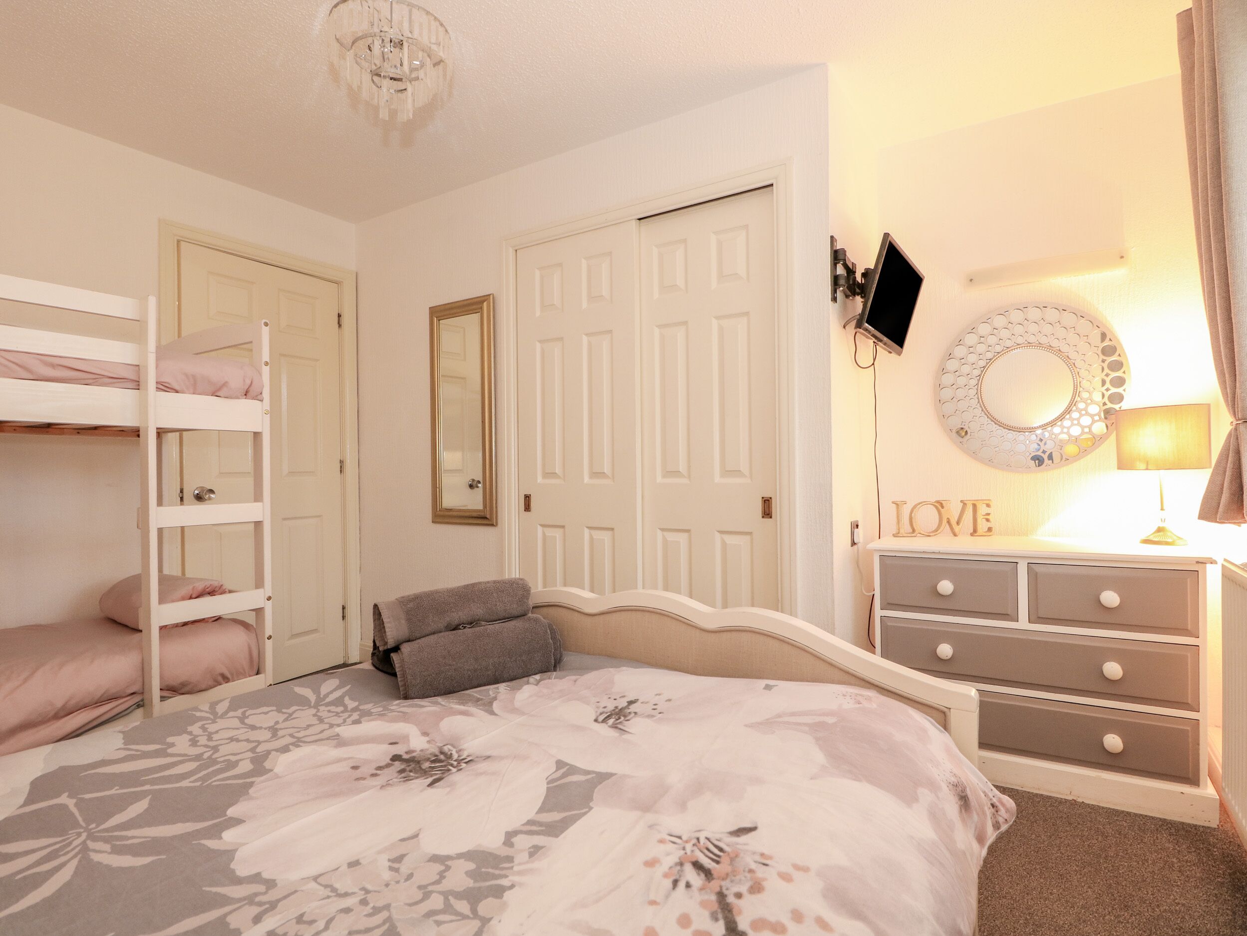 A bedroom with a bunk bed, a single bed, a dresser, a mirror, and a wall-mounted TV.