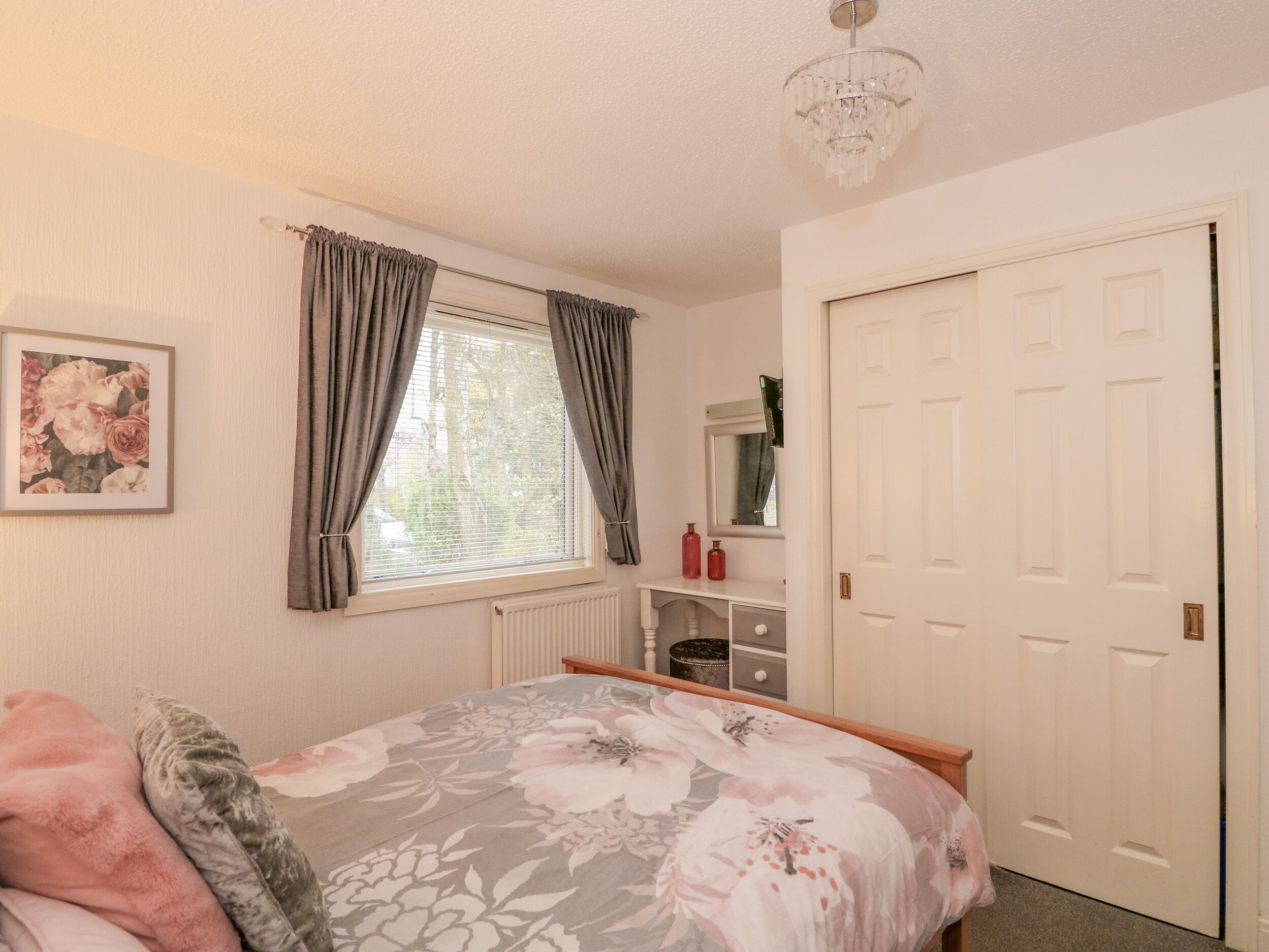 A bedroom with a bed, a window with curtains, a radiator, a mirror, and a door.
