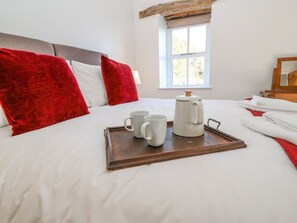 A neatly made bed with white bedding and red pillows, a tray with two white mugs and a white coffee pot, and a window with a view of greenery. - The Cottage, Beeston Hall (Sowerby Bridge)