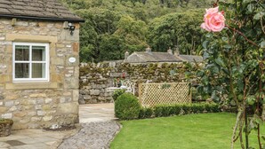 A stone building with a window and a stone wall with a lattice fence. - The Bothy (Skipton)