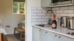 A kitchen with white cabinets, a stainless steel sink, and a microwave. There's a bottle of wine and a glass on the counter. - The Bothy (Skipton)