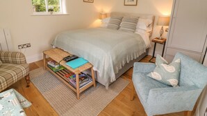A bedroom with a bed, bedside tables, a chair, a small table with books, a window, and a door. - The Bothy (Skipton)