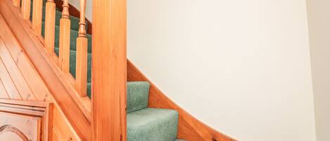 A wooden staircase with green carpeted steps and wooden railings.