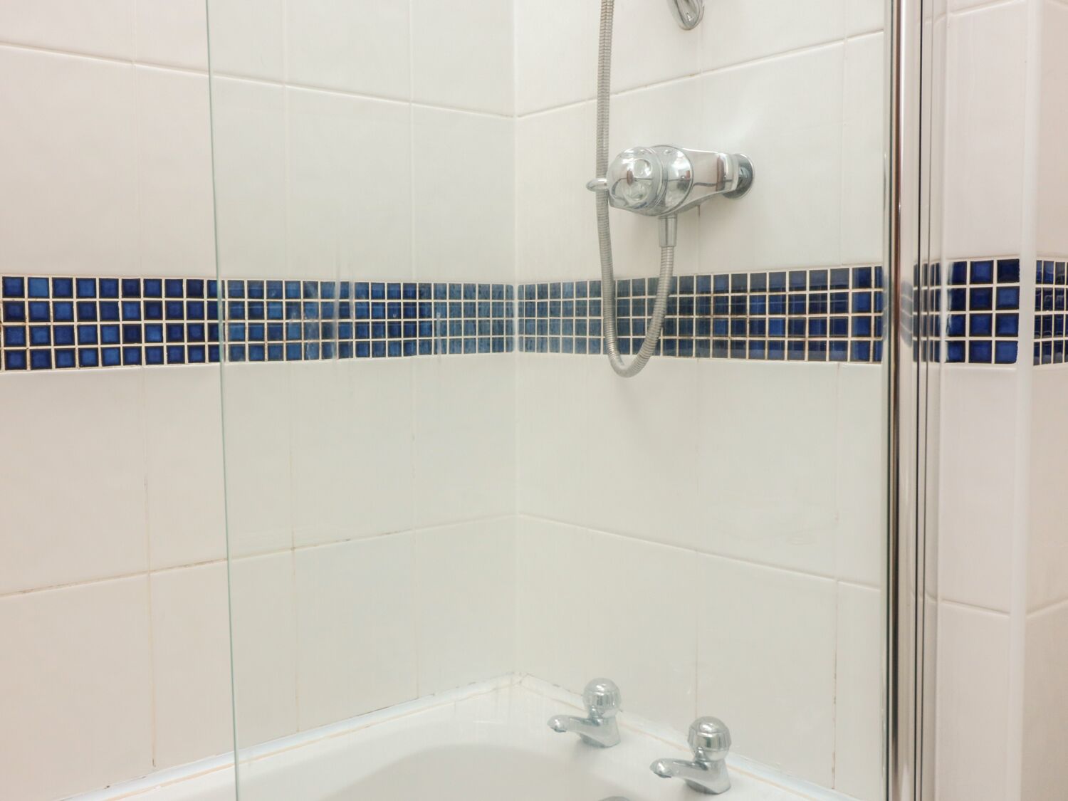 A bathroom with white tiles, a glass shower enclosure, and a blue-tiled accent strip.