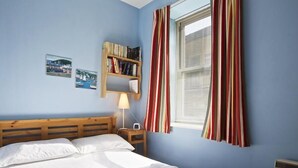 A bedroom with a bed, a bedside table with a lamp, a bookshelf, and a window with curtains. - Columbine (Dartmouth)