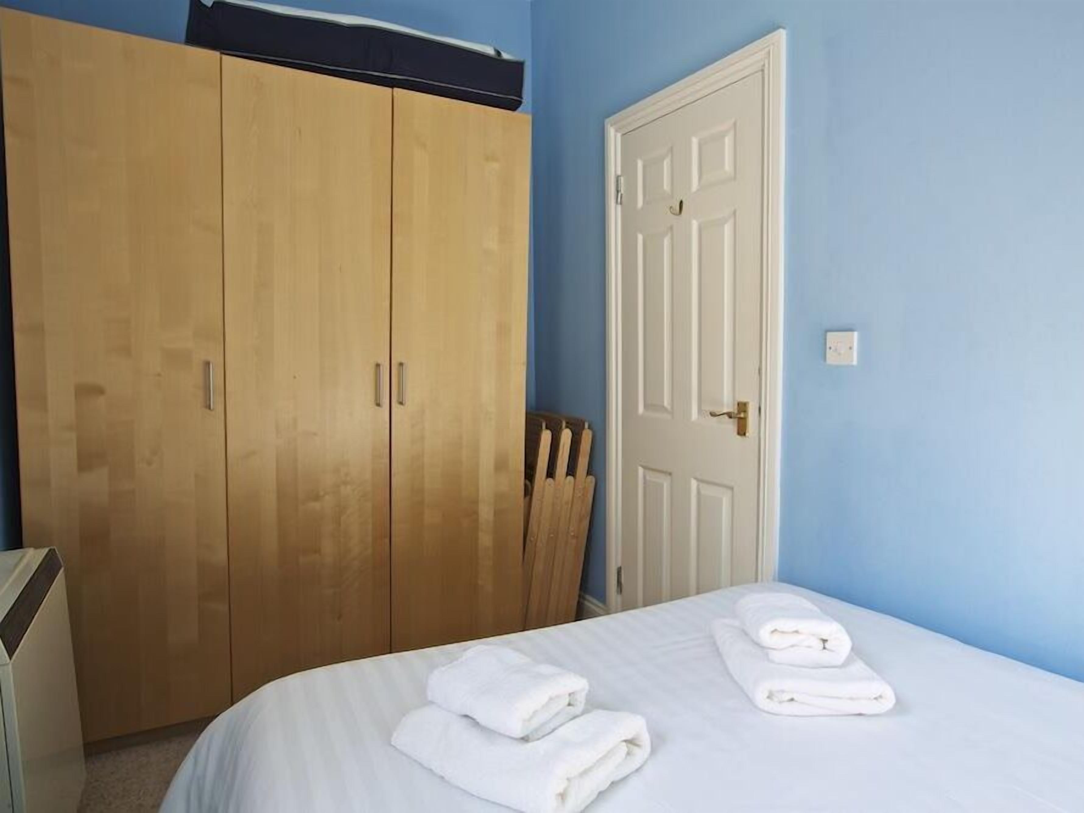 A bedroom with a bed, white towels, a wooden wardrobe, and a white door.