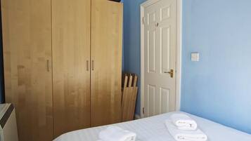 A bedroom with a bed, white towels, a wooden wardrobe, and a white door.
