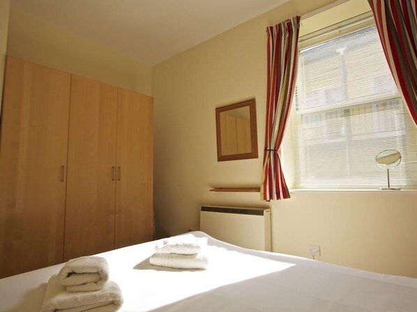 A bedroom with a bed, a wooden wardrobe, a mirror, and a window with curtains. - Columbine (Dartmouth)