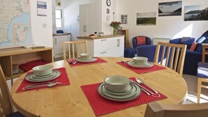 A dining area with a wooden table set for four, surrounded by chairs. There is a kitchen visible in the background with white cabinets and a countertop. - Columbine (Dartmouth)