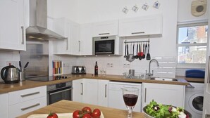 A modern kitchen with white cabinets, a microwave, a toaster, and a sink. There are tomatoes on a cutting board and a bowl of salad on the counter. - Columbine (Dartmouth)