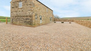 A stone building with a sloped roof, a gravel driveway, and a stone wall in the background.