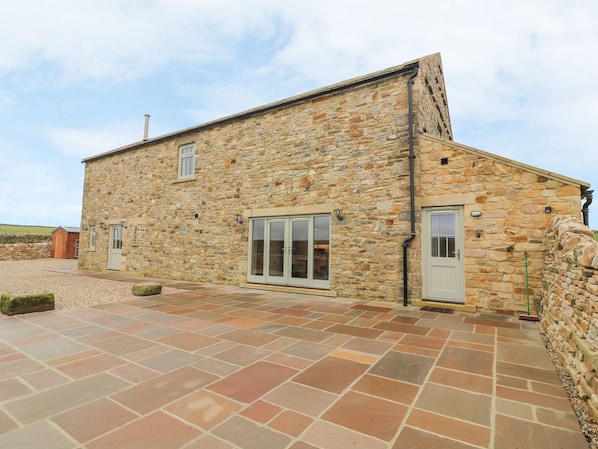A stone building with a sloped roof, a gravel driveway, and a stone wall.