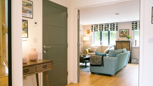 A hallway leading to a living room with a sofa, a lamp, and a window with a view. - Sidings at Brunel Two (Lostwithiel)