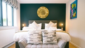 A modern bedroom with a bed, grey upholstered bench, and a decorative wall piece. - Sidings at Brunel Two (Lostwithiel)