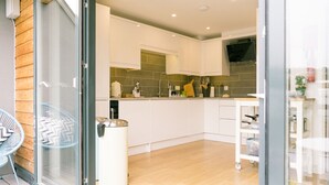 A modern kitchen with white cabinets, a wooden floor, and a glass door leading to a balcony. - Sidings at Brunel Two (Lostwithiel)