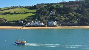 A coastal scene with a boat on the water, a sandy beach, and houses on a hillside. - Crab Cottage (Salcombe)