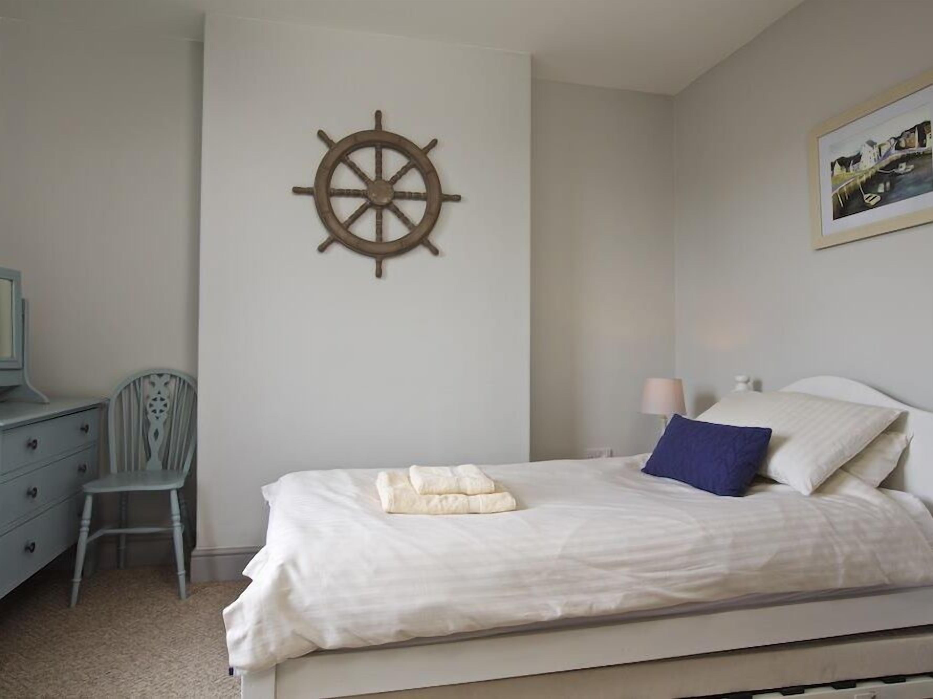 Un dormitorio con cama, una silla, un escritorio y un timón de barco en la pared.