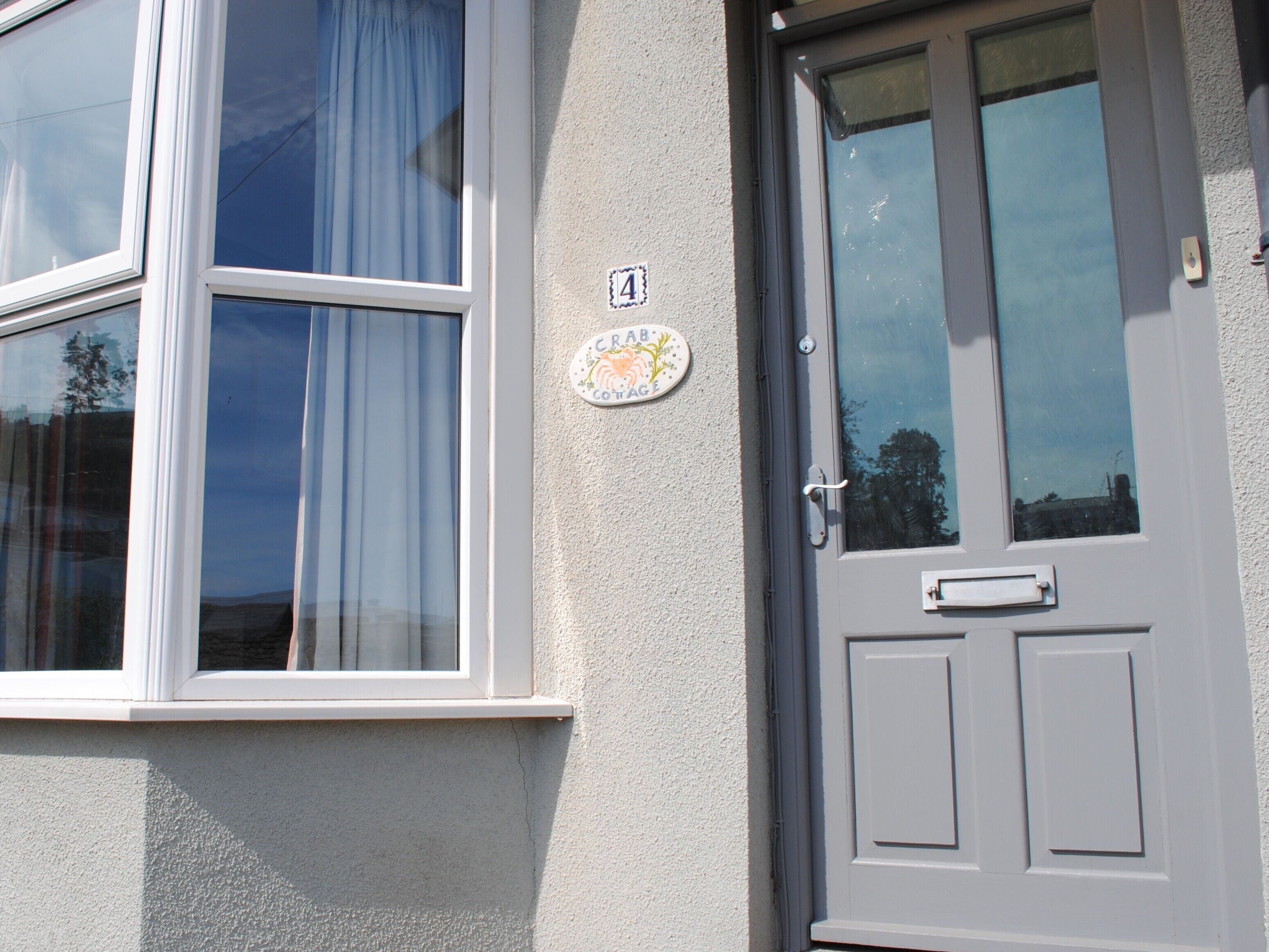 A house with a grey door and a window with white frames. There is a plaque on the wall next to the door.