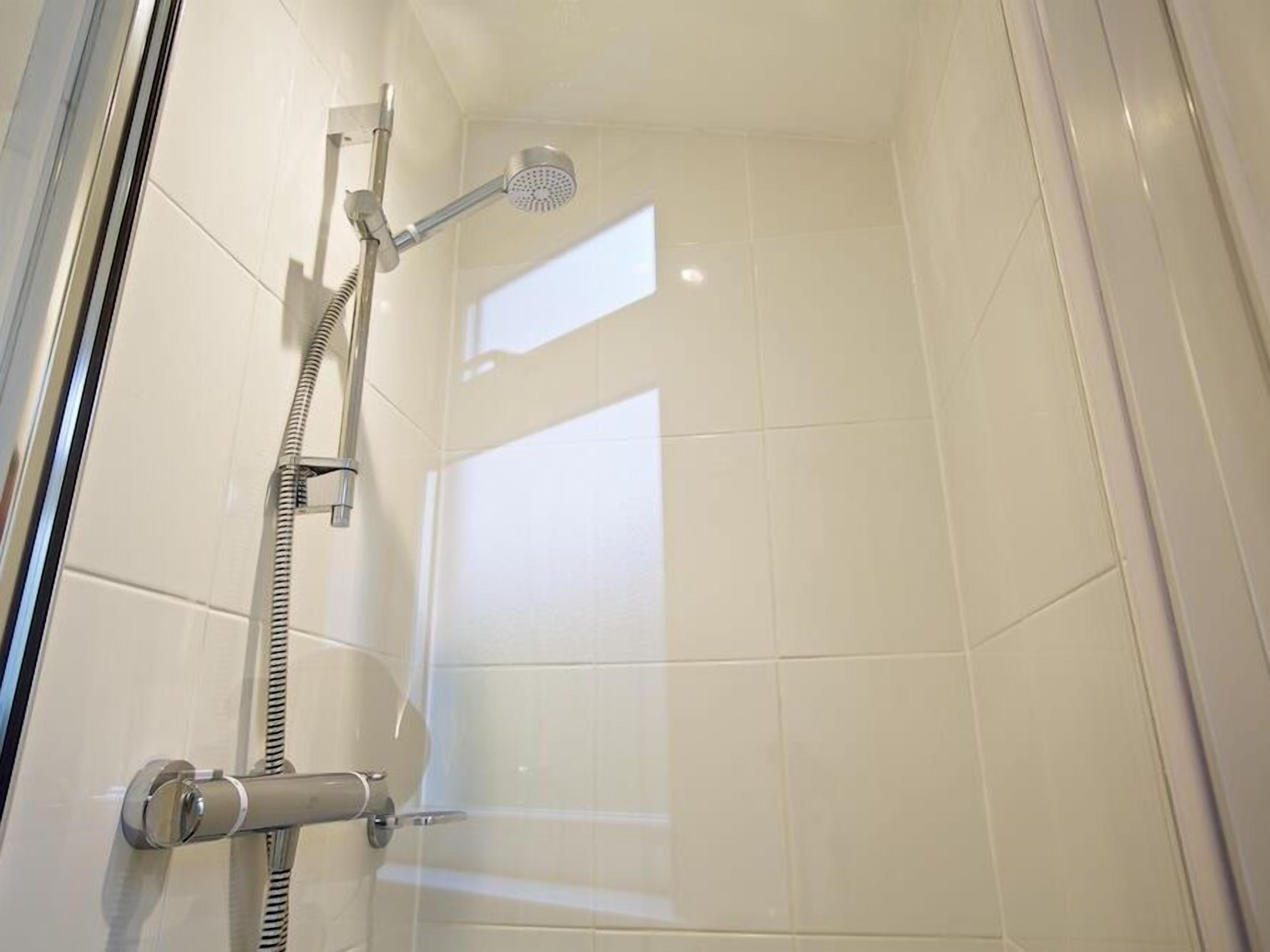 Une douche équipée d’un pommeau de douche à main et d’un robinet mural.
