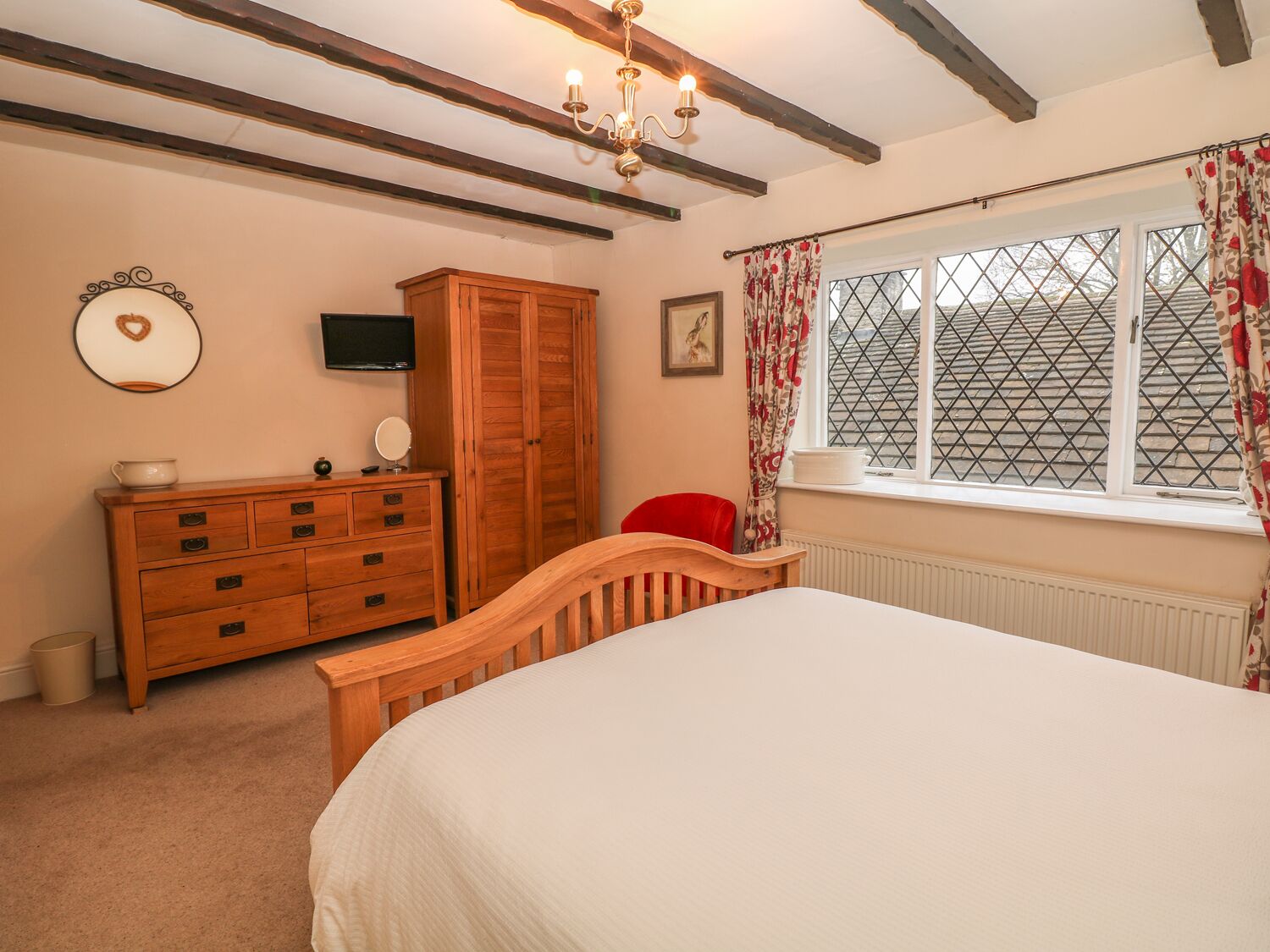 A bedroom with a wooden bed, a dresser, a television, and a window with patterned curtains.