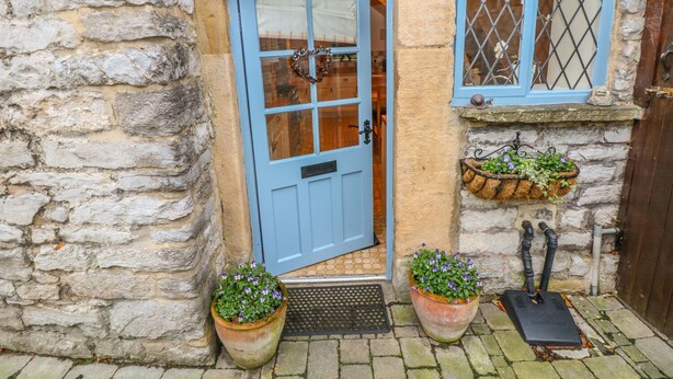 A stone building with a blue door, two potted plants, and a window with a metal grille. - Laburnum Cottage (Hope Valley)