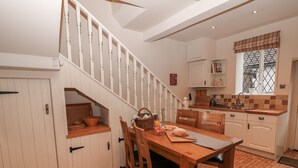 A kitchen with a wooden table, chairs, a staircase, and a window with a view. - Laburnum Cottage (Hope Valley)