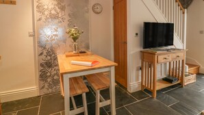 A cozy living room with a wooden table, a TV, and a staircase. - Crift Farm Cottage (Bodmin)