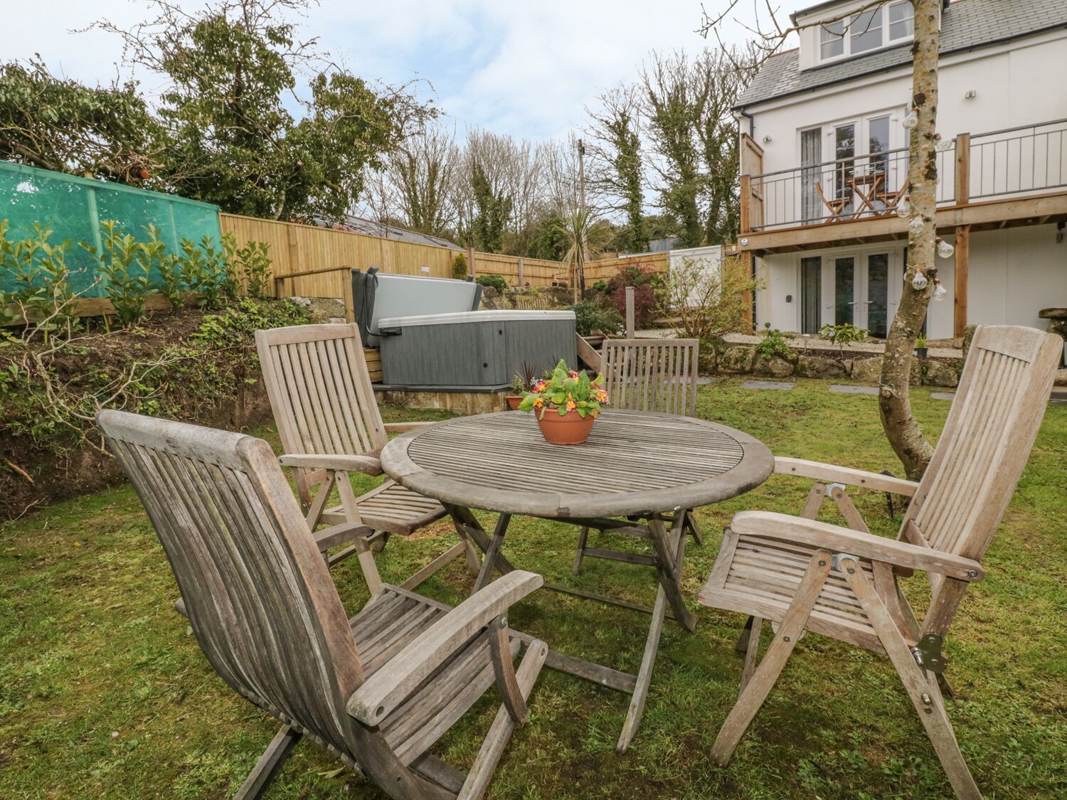 Une table ronde en bois, entourée de quatre chaises, avec une plante en pot et un barbecue dans un jardin.