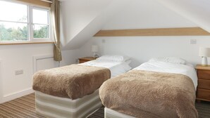 A bedroom with two beds, a window with curtains, a wooden headboard, and a striped carpet. - Crift Farm Cottage (Bodmin)