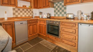 A kitchen with wooden cabinets, a dishwasher, an oven, and a toaster. - Crift Farm Cottage (Bodmin)