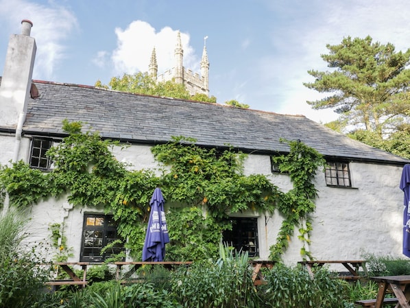A white building with ivy, a chimney, and a tower in the background. - Crift Farm Cottage (Bodmin)