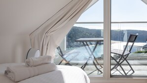 A bedroom with a large window, a bed with folded towels, and a view of a waterfall and greenery outside. - 4 Blue View (Salcombe)