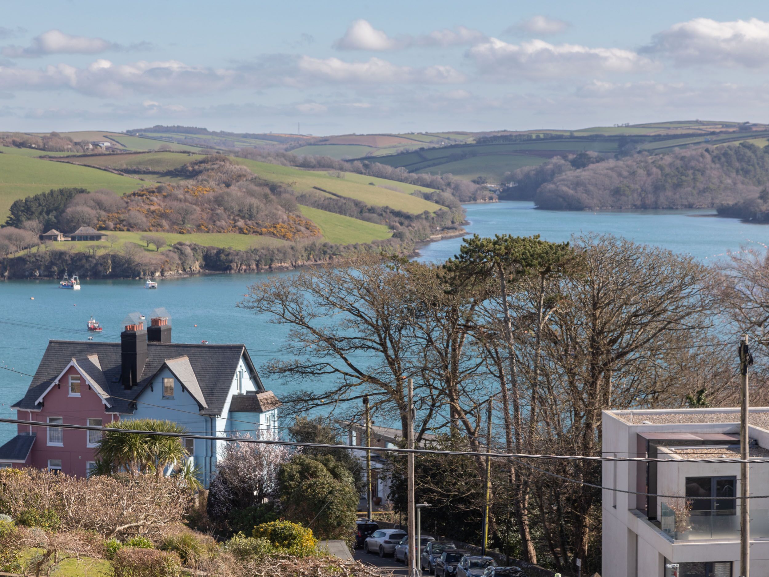 A coastal town with houses near a body of water, a modern building, and a hilly landscape in the background.