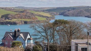 A coastal town with houses near a body of water, a modern building, and a hilly landscape in the background.