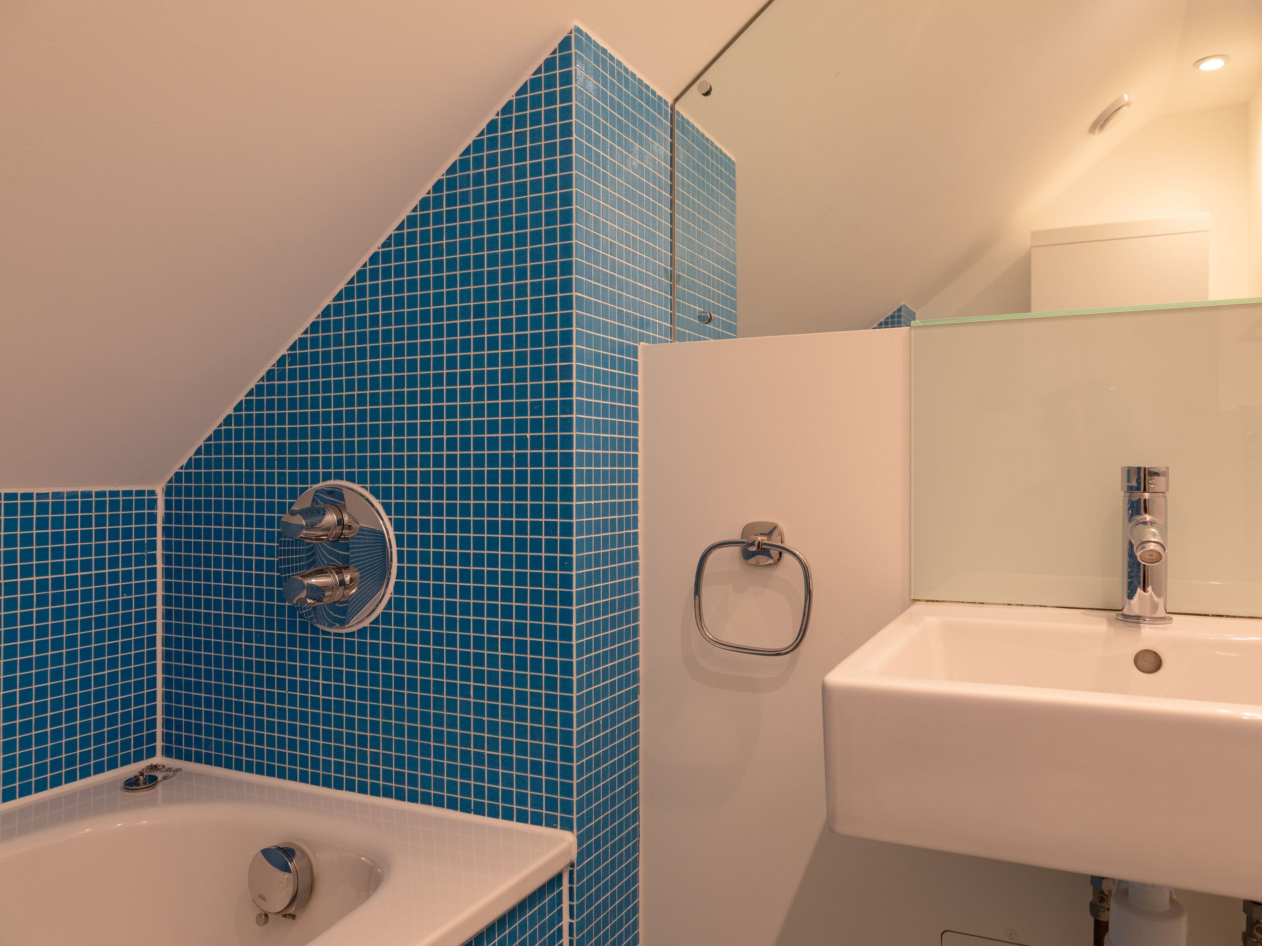 A bathroom with a blue-tiled shower wall, a white sink, and a glass-enclosed mirror.
