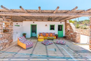 A covered outdoor seating area with stone walls, a wooden pergola, and colorful cushions.