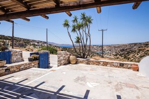 A covered outdoor area with a view of the sea, stone walls, and palm trees.