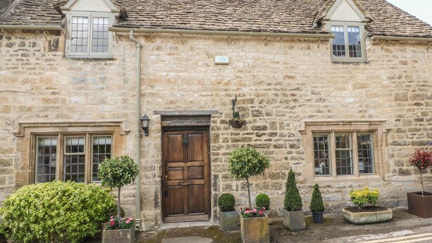 A stone building with a wooden door, windows, and potted plants. - Bull Cottage (Burford)