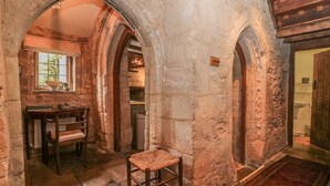 A stone-walled room with a wooden chair, a small table, and a window. - Bull Cottage (Burford)