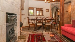 A dining area with a wooden table and chairs, a fireplace, and a red sofa. - Bull Cottage (Burford)