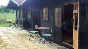 A log cabin with a patio area featuring a table and chairs, a small garden, and a wooden door. - The Theberton Lion (Leiston)