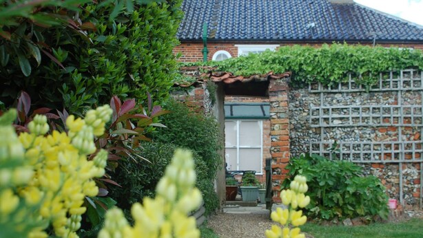 A garden leading to a brick house with a tiled roof and a small window. - The Theberton Lion (Leiston)