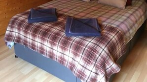 A cozy wooden cabin room with a bed, a nightstand, and a wall with a floral painting and a sign. - The Theberton Lion (Leiston)