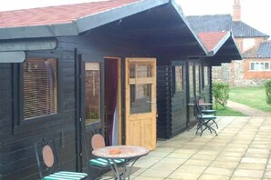 A wooden cabin with a porch, a table, and two chairs. - The Theberton Lion (Leiston)